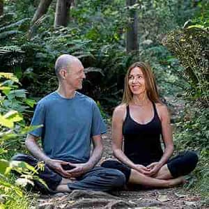 Bernie Clark and Nathalie Keiller sitting next to each other crossed legged in a forest for an online meditation course. Vedic meditation training
