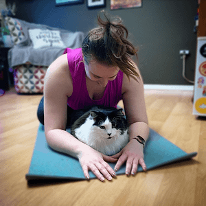 Jennifer, a caucasian women, online yoga teacher in her home with her black & white cat.