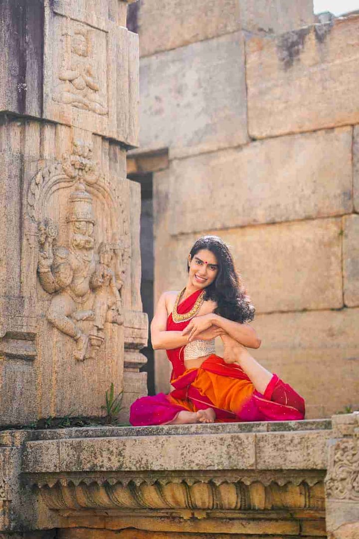 young woman from india shes wearing red clothing doing a mermaid yoga pose her name is Carolyn Theresa Simon