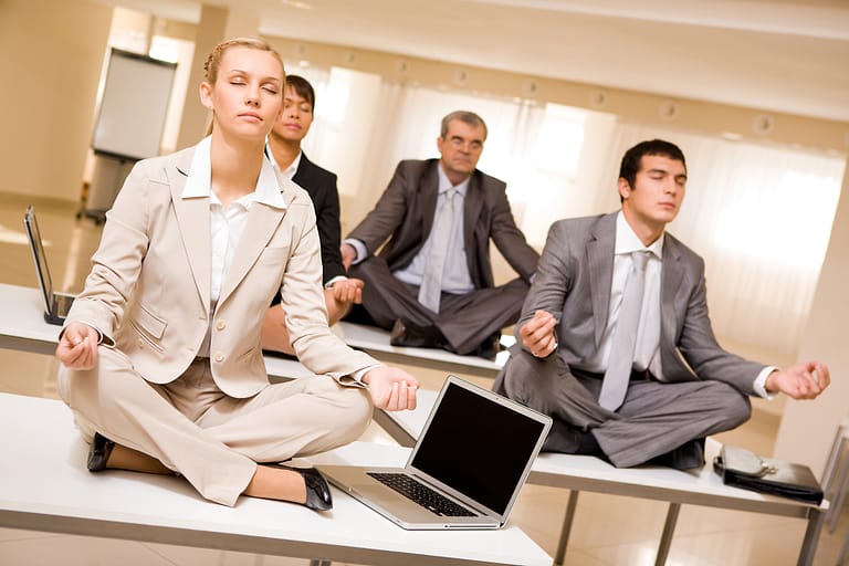 4 office workers sitting on their desk. meditating getting the benefits of yoga in the workplace